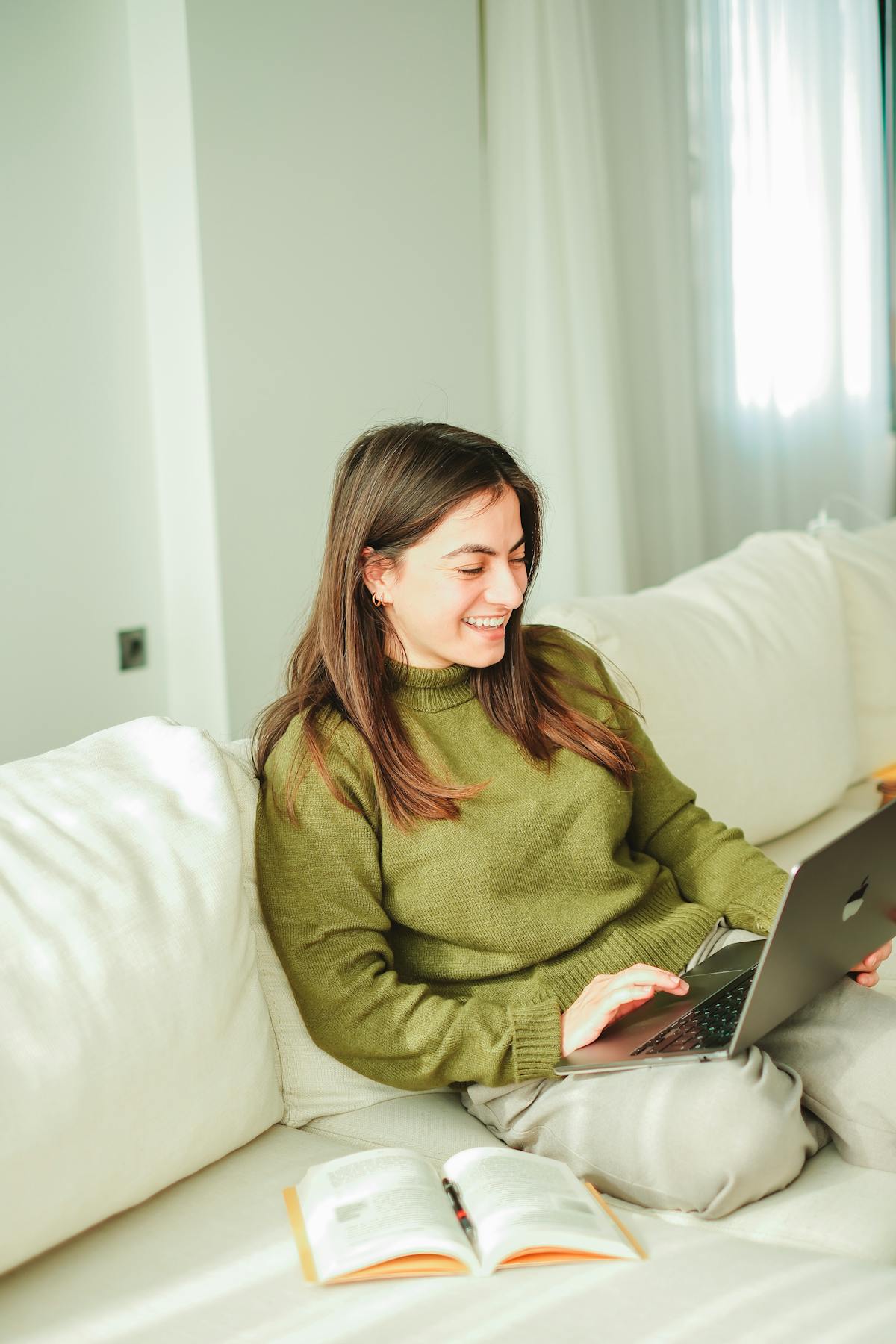 woman smiling in green shirt reading from laptop on couch 